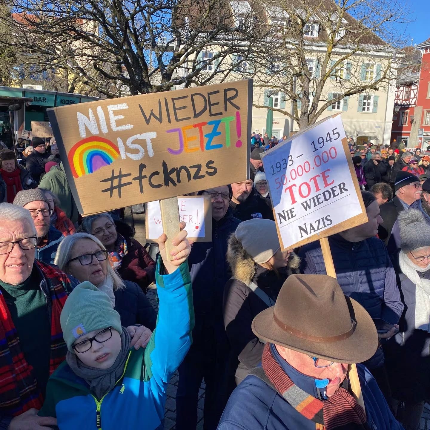 Größere Menschenmenge bei Demonstration. Im Vordergrund Schilder, die mit Botschaften gegen Rassismus beschriftet sind.